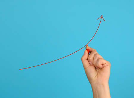 female hand draws a red up arrow on a blue background. The concept of increasing profits, the...