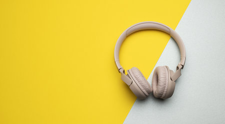 pink wireless headphones on a gray-yellow background, top view. Modern gadget for listening to musicの写真素材