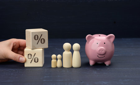 wooden family figurines and pink ceramic piggy bank on blue background. Concept of accumulating cash for buying a house and a car, money in the bank at interest, safe storageの写真素材