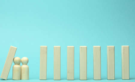 figures of men restrain the falling of wooden blocks, the effect of dominoes on a blue background. concept of teamwork, the ability to prevent the consequences of the influence of external sources on the businessの写真素材