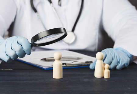 family doctor holds a magnifying glass over a wooden figurine. Medical research concept, treatment methods. The need for medical insuranceの写真素材