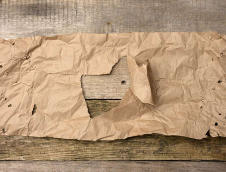 torn sheet of brown paper with a hole on a wooden background from boardsの写真素材