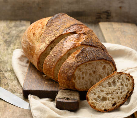 baked round bread made from white wheat board on wooden board, loaf cut into pieces, close up