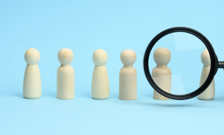 wooden figures of men stand on a blue background and a black magnifying glass. Recruitment concept, search for talented and capable employees, career growthの写真素材