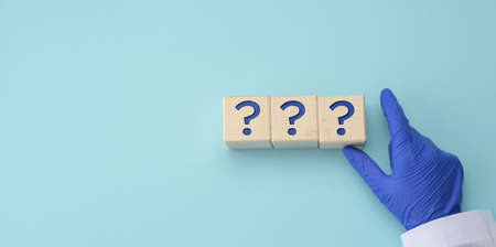 a hand in a blue medical glove holds cubes with question marks on a blue background. The concept of...