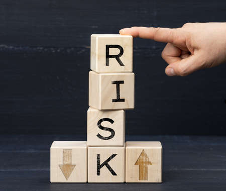 wooden cubes with the inscription risk on a blue background. Risk reduction concept, reinsurance. How to avoid losses, unknown new beginnings in business and lifeの写真素材