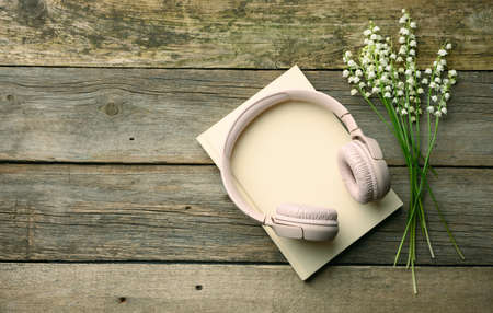 bouquet of blooming lilies of the valley and wireless headphones and a closed notepad on a wooden background. Top viewの写真素材
