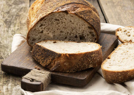 baked round bread made from white wheat board on wooden board, loaf cut into pieces, close up