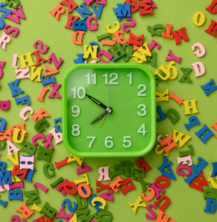 square alarm clock and multicolored wooden letters of the english alphabet on a green background, top viewの写真素材