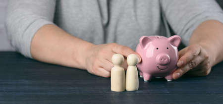 wooden figurines of little men family on the background of a man with a piggy bank. The concept of...