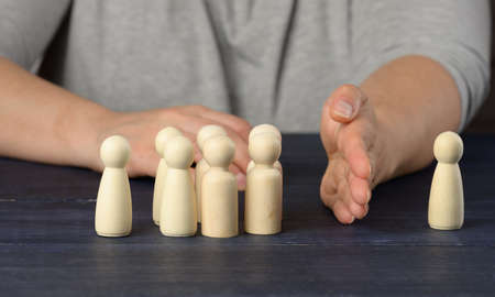 female hand between wooden figures of men on a blue background. The concept of a quarrel, disagreement in the team. The need for reconciliation, protection of the oppressedの写真素材