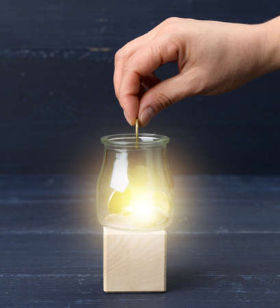 female hand throws coins into a transparent glass jar. The concept of poverty, savings and subsidies...