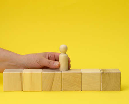 female hand holds a wooden figurine of a man and puts on a cube. Promotion concept, coaching and...