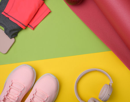 red sports mat pair of pink sneakers, wireless headphones, a smartphone on a green yellow background. Things and gadgets for sports, flat layの写真素材
