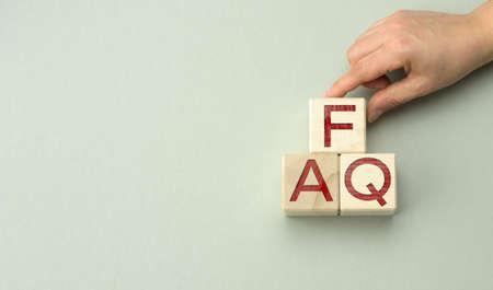 inscription FAQ (frequently asked questions) on wooden blocks on a gray background. QA concept, help and tips, hand holds cubes, copy spaceの写真素材