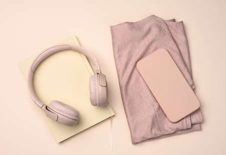 pair of pink sneakers, wireless headphones, a smartphone and a smart watch on a pink background....