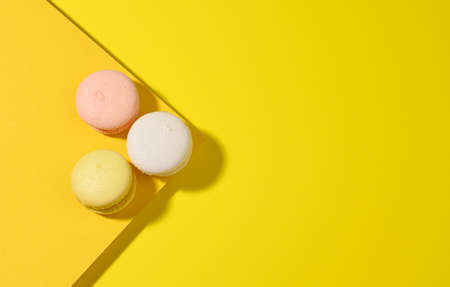 round multicolored macarons on a yellow background with a shadow on a yellow background. Gourmet almond flour dessert, top viewの写真素材