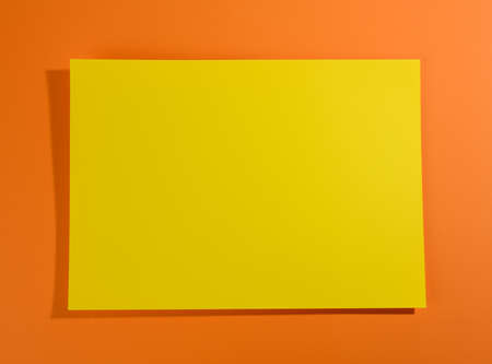 blank yellow sheet of paper on orange background with shadow, abstract backdrop for inscription,...