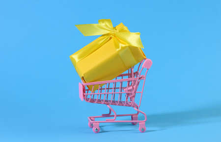 yellow gift box with a silk bow in a miniature metal trolley on a light blue background. Party Backdrop, Surprise, Seasonal Saleの写真素材