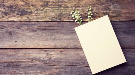 notebook with blank white sheets and a bouquet of blooming lilies of the valley on a wooden table from gray boards, top viewの写真素材