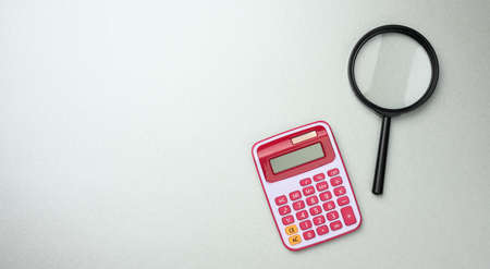 black plastic magnifier and pink calculator on gray background, budget planning, profit counting,...