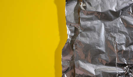 crumpled sheet of gray foil for packaging products with torn edges on a yellow background, flat lay, copy spaceの写真素材