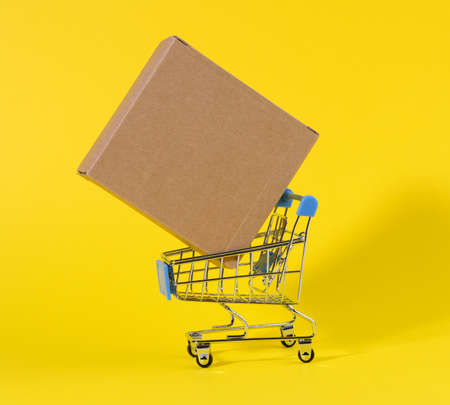 miniature trolley with brown cardboard box on yellow background. The concept of delivery of goods, online shoppingの写真素材