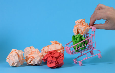 hand holds a miniature metal cart with mint paper balls on a blue background. Concept for buying ideas, new creative ideasの写真素材