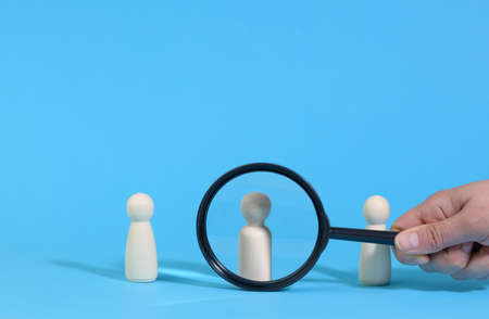 wooden figures of men stand on a blue background and a black magnifying glass. Recruitment concept, search for talented and capable employees, career growthの写真素材