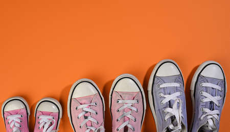many multi-colored well-worn textile sneakers of different sizes on a orange background, top view, concept family and team, friendship, copy spaceの写真素材