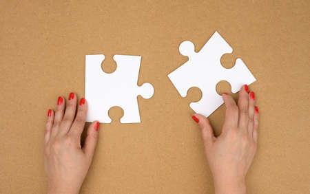 two empty paper white pieces of puzzles in female hands, puzzle connected, brown background, top...