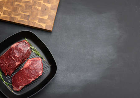 two raw pieces of beef in a black square grill pan, steaks on a black background, top view, copy spaceの写真素材