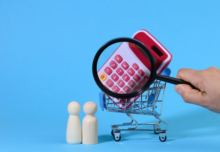 miniature metal shopping cart with calculator and wooden family. Hand with a magnifying glass, the concept of budget control, spending on purchases, saving moneyの写真素材