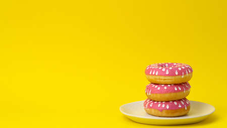 stack of pink donuts with icing on a yellow background, copy spaceの写真素材