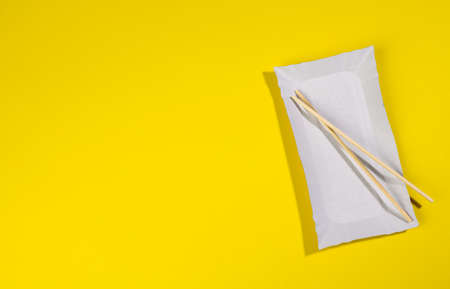 paper rectangular plates wooden chopsticks on yellow background, top view