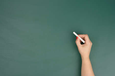 hand holds a piece of white chalk on the background of an empty green chalk board, presentation concept, back to schoolの写真素材