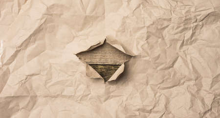 torn sheet of brown paper with a hole on a wooden background from old boardsの写真素材