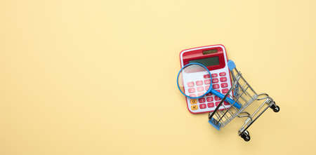 pink plastic calculator in a miniature pink trolley on a yellow background. Budget planning concept, savings counting, cost control, flat layの写真素材