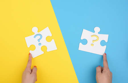 female hand holds a fragment of a white large puzzle on a yellow blue background, concept of finding...