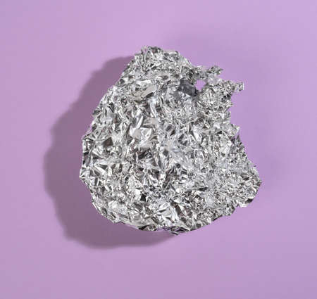crumpled piece of gray foil with shadow on purple, top viewの写真素材