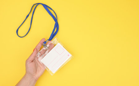 female hand holds transparent plastic badge on a blue lanyard on a yellow background, copy spaceの写真素材