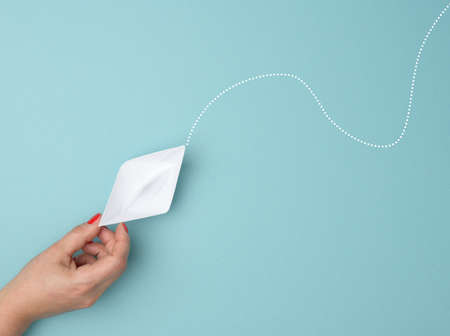 female hand hold a white paper boat on a blue background. Mentoring and support concep, top viewの写真素材