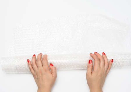 female hand holding crumpled piece of polyethylene with air bubbles on a white background, packing...