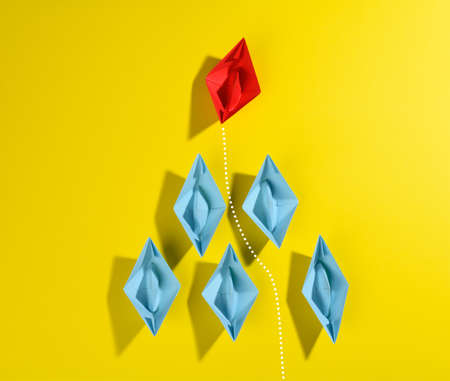 group of blue paper boats and one red led on a yellow background. Strong leader concept, growth of...