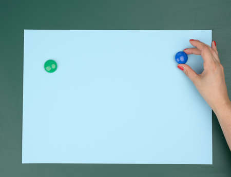 two female hands fix a blue blank sheet of paper on a magnetic board, place for an inscription
