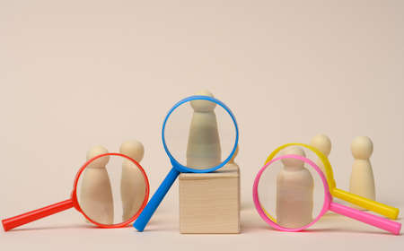wooden figures of men stand on a beige background and a plastic magnifying glass. Recruitment concept, search for talented and capable employees, career growthの写真素材