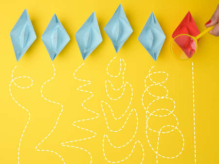 female hand holds a magnifying glass over a row of paper boats on a yellow background. Talent search concept, recruiting, recruitment interviewsの写真素材