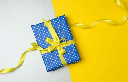 blue gift box tied with a yellown silk ribbon on the gray background, top view. Festive backdropの写真素材