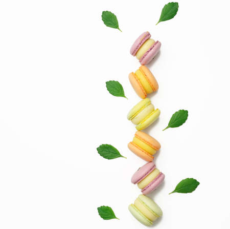 baked multicolored macarons lie in a row on a white background, green mint leaves, top viewの写真素材