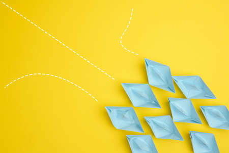 group of blue paper boats with different paths on yellow background, path choice concept. Teamwork